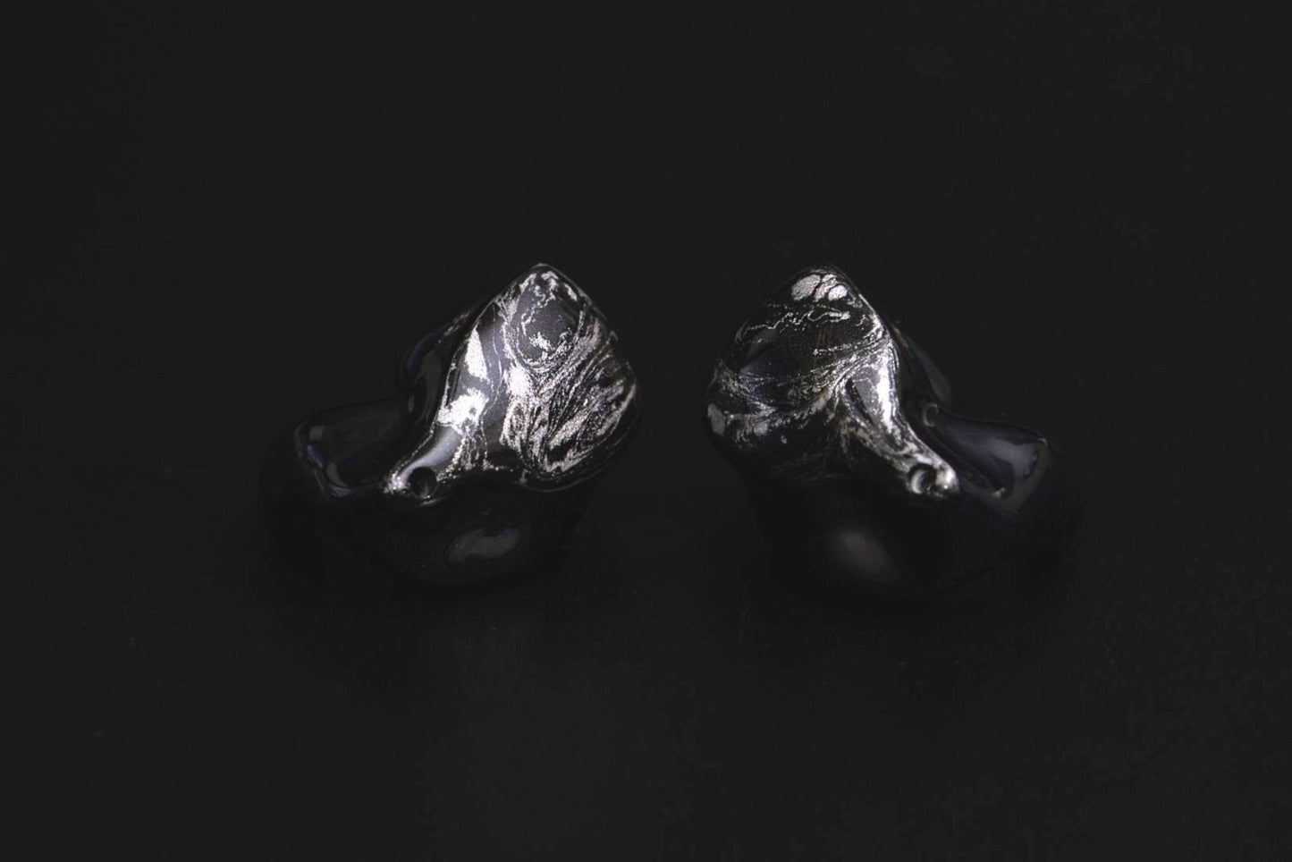 A pair of black custom in-ear monitors with a distinctive design, featuring a black and silver color scheme and a metallic finish. 