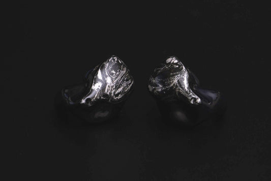 A pair of black custom in-ear monitors with a distinctive design, featuring a black and silver color scheme and a metallic finish. 