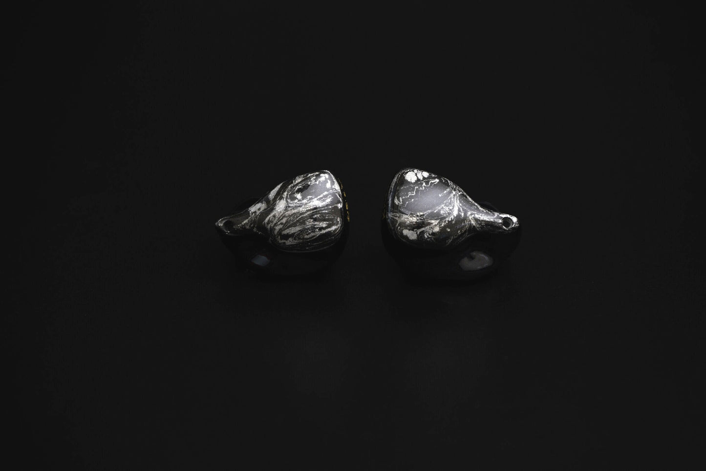 A pair of black custom in-ear monitors with a distinctive design, featuring a black and silver color scheme and a metallic finish. Alternate view