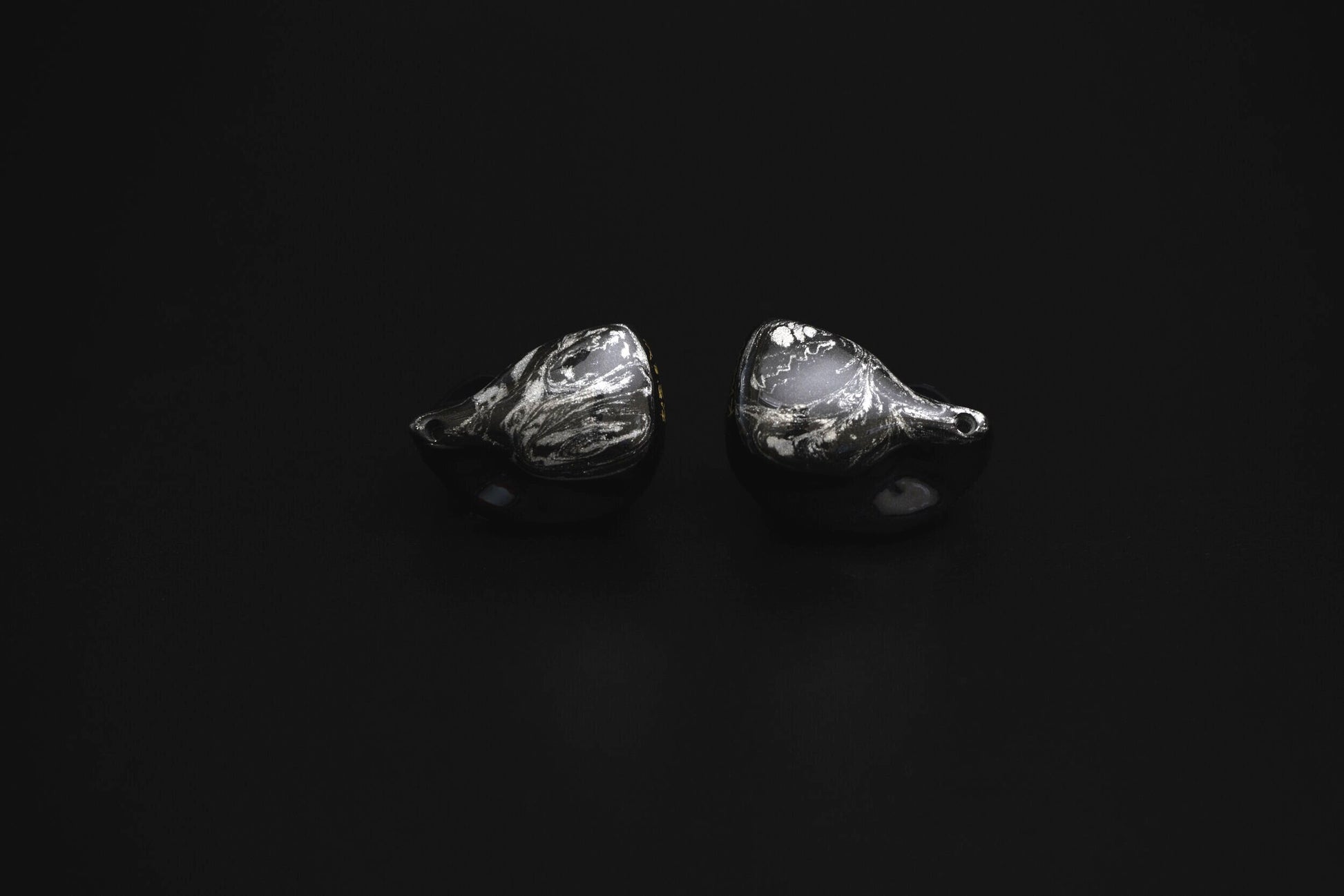 A pair of black custom in-ear monitors with a distinctive design, featuring a black and silver color scheme and a metallic finish. Alternate view