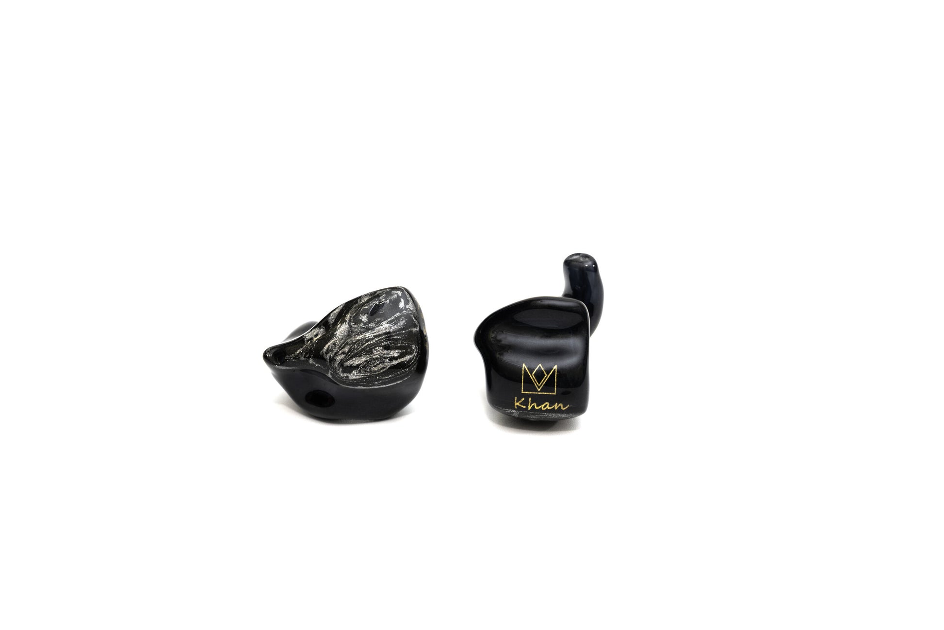 A pair of black custom in-ear monitors with a distinctive design, featuring a black and silver color scheme and a metallic finish. The right in-ear monitor is flipped and reversed to show a gold Noble logo and cursive "Khan" on a white background.