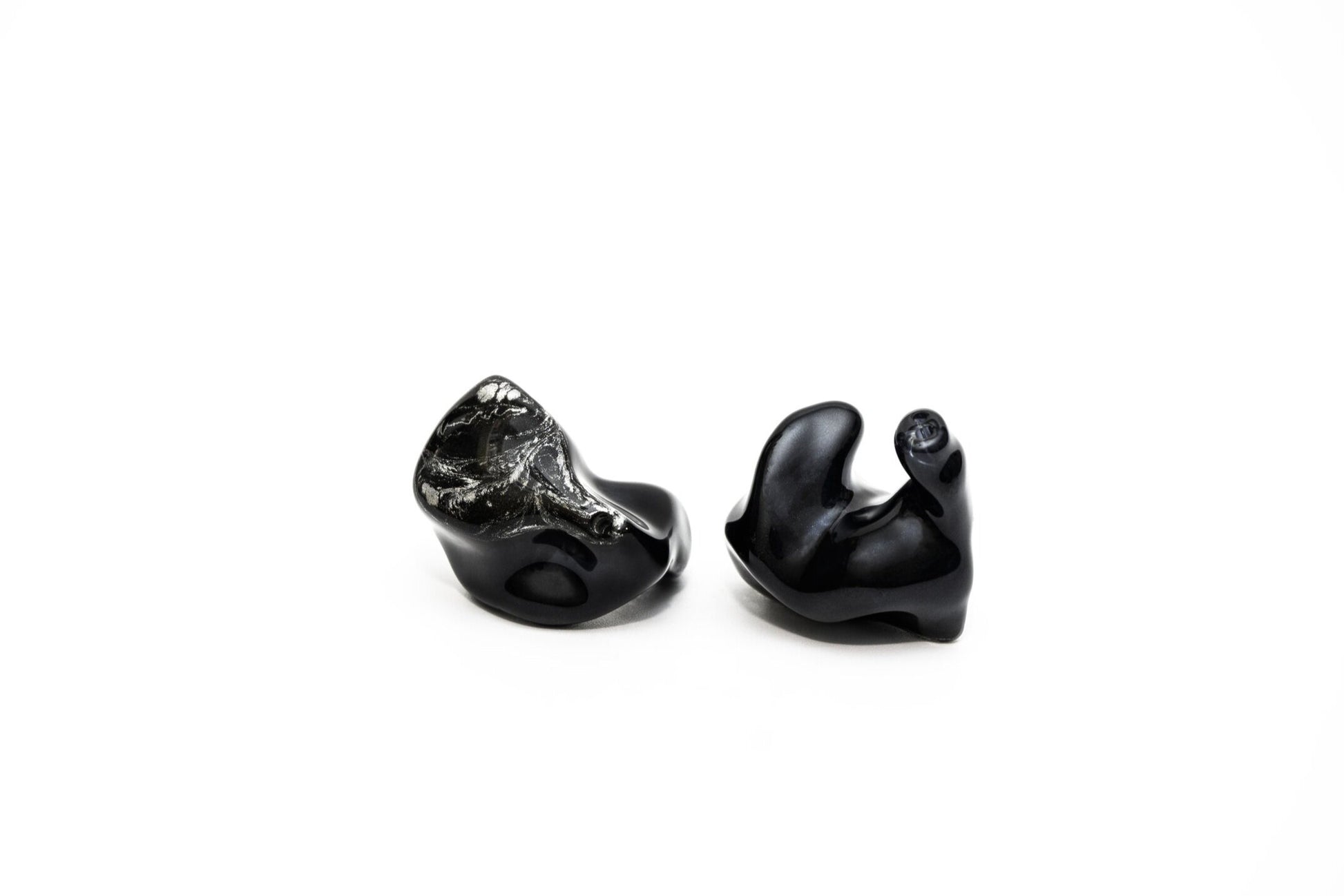 A pair of black custom in-ear monitors with a distinctive design, featuring a black and silver color scheme and a metallic finish. Right in-ear monitor 
is flipped to show contours. 